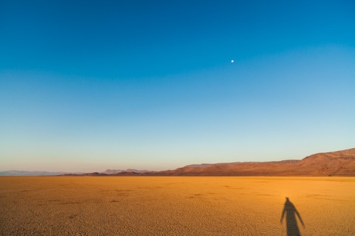 The shadow of a tall man creeps eerily across the cracked playa of the Alvord Desert in Southeast Oregon as the moon looms above.